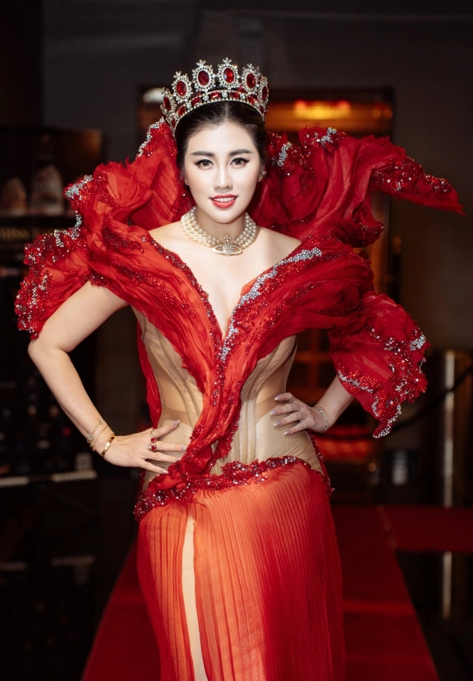 Cô đội vương miện, kết hợp vòng cổ ngọc trai và trang sức bắt mắt. Kiểu tóc uốn sóng nhẹ và lối trang điểm tông ấm giúp người đẹp tôn nét thanh lịch.